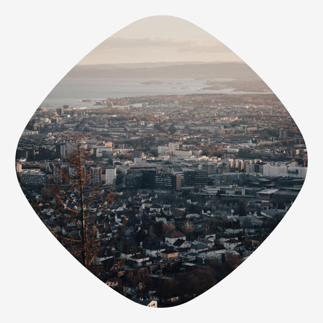 Utsikt over Oslo by i skumringslys, med tett bebyggelse, fjorden og øyer i bakgrunnen.