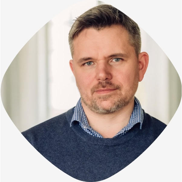Portrett av Henrik Pyser Libell, rådgiver i Stiftelsen Fritt Ord, i stipete skjorte og blå genser, fotografert innendørs med mykt dagslys.