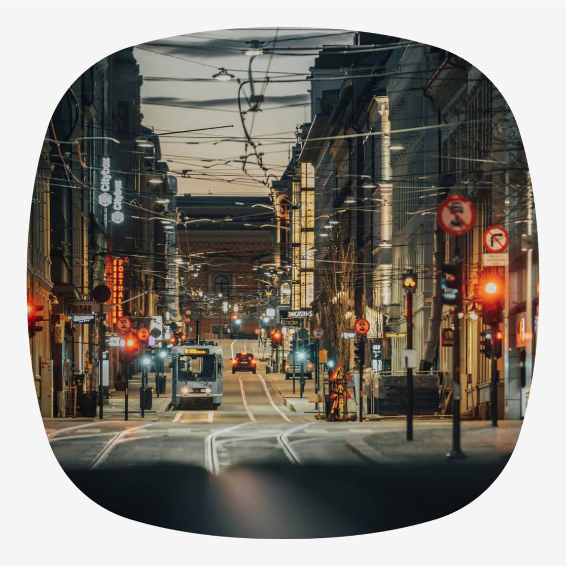 En gate i Oslo sentrum ved skumring, med trikkeskinner, opplyste bygninger og lys fra trafikken.