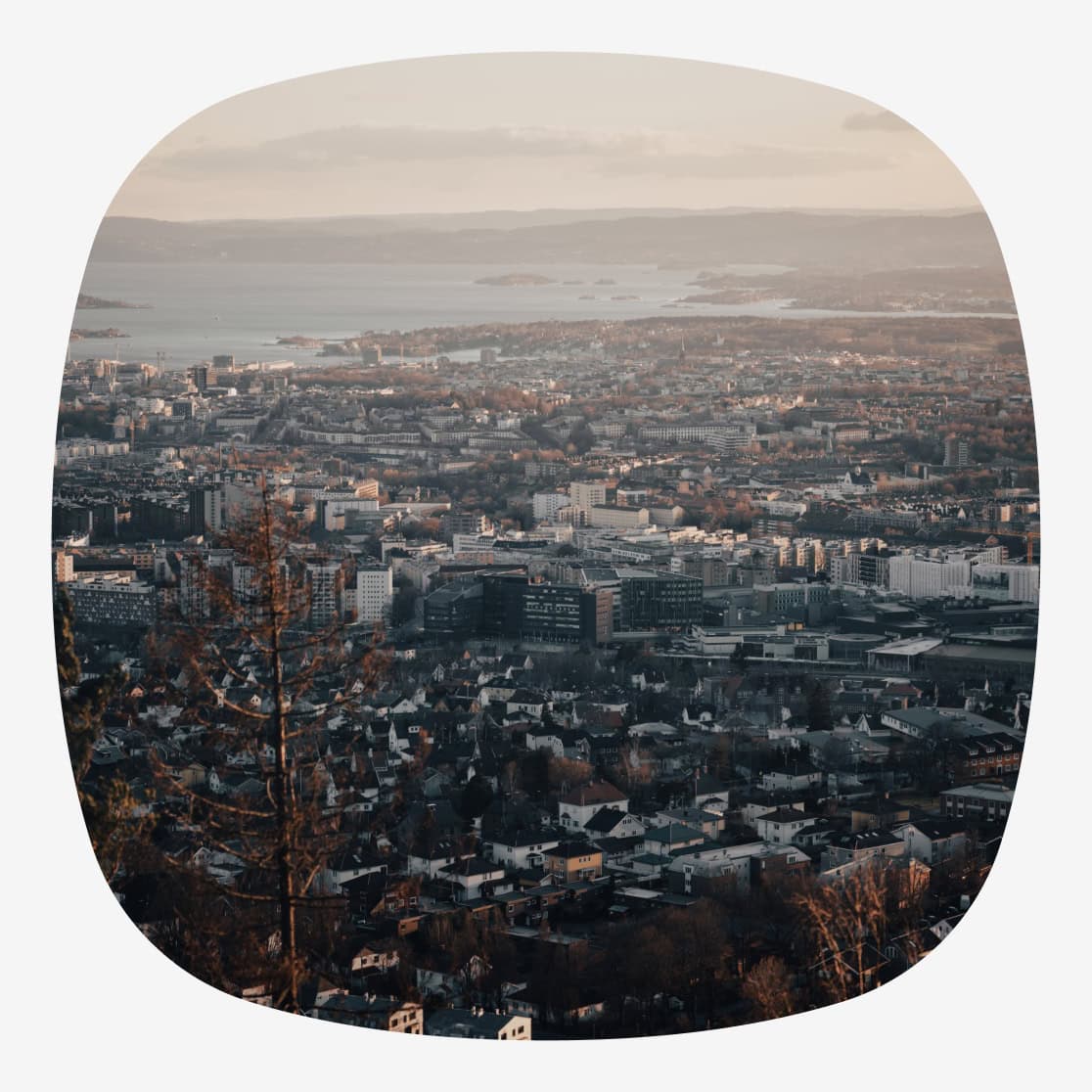 Utsikt over Oslo by i skumringslys, med tett bebyggelse, fjorden og øyer i bakgrunnen.