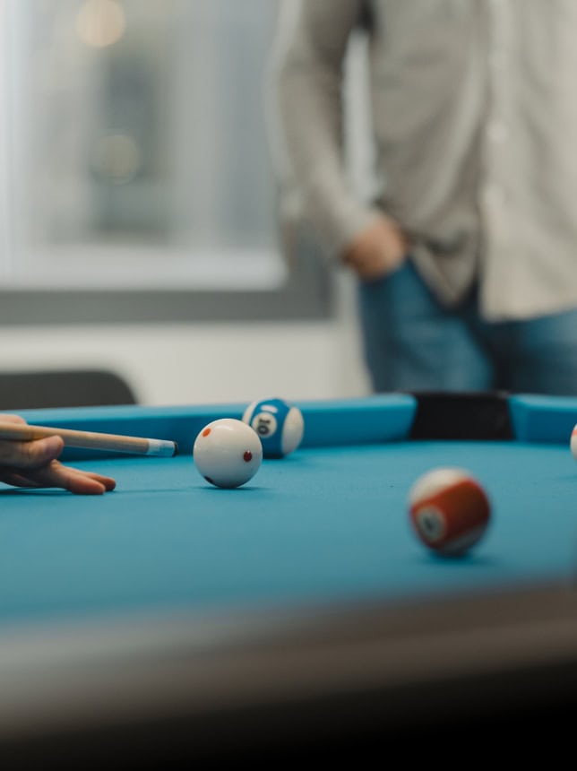 En biljardscene der en ball ligger klar på bordet, med en person delvis synlig i bakgrunnen.